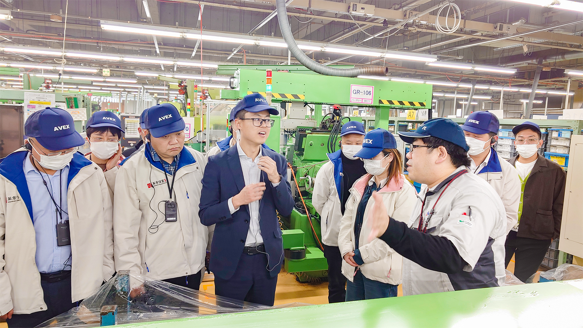 A man giving a tour at the manufacturing plant and a group of visitors
